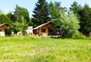 Safari tent with bathroom at Campsite La Faz in France, set among green trees and a grassy meadow.