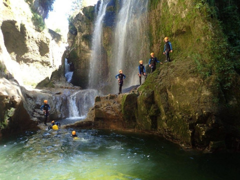 Persone con caschi esplorano una cascata e nuotano al Campsite «La Faz» in Borgogna-Franca Contea, Francia.