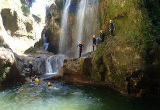 Persone con caschi esplorano una cascata e nuotano al Campsite «La Faz» in Borgogna-Franca Contea, Francia.