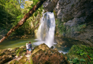 Due persone osservano una cascata immersa nella natura lussureggiante vicino a Orgelet, Francia.