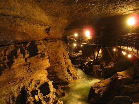 Grotta illuminata con fiume e passerella al Campeggio La Faz in Bourgogne-Franche-Comté, Francia.