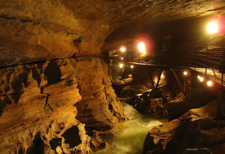 Grotta illuminata con fiume e passerella al Campeggio La Faz in Bourgogne-Franche-Comté, Francia.