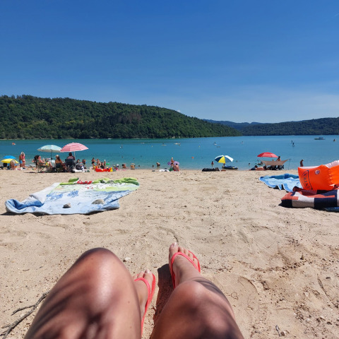 Scena rilassante in spiaggia al Campeggio La Faz con gente, ombrelloni colorati e acqua azzurra sullo sfondo.