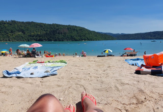 Scena rilassante in spiaggia al Campeggio La Faz con gente, ombrelloni colorati e acqua azzurra sullo sfondo.