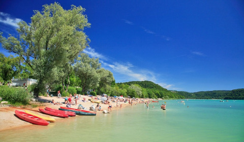 Spiaggia su un lago vicino a Orgelet, Bourgogne-Franche-Comté, Francia, con persone, canoe e alberi verdi.
