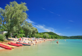 Spiaggia su un lago vicino a Orgelet, Bourgogne-Franche-Comté, Francia, con persone, canoe e alberi verdi.