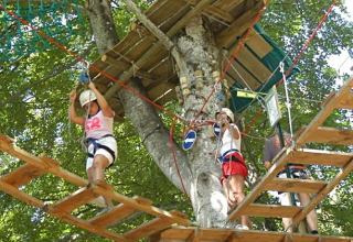 Bambini con caschi e imbragature si divertono su un percorso avventura sugli alberi al campeggio La Faz, Bourgogne, Francia.