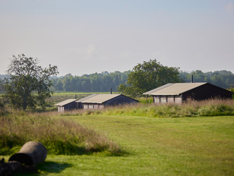 Drie rustieke hutten omringd door gras en bomen op BoerenBed College Farm vakantiepark in Oost-Engeland.