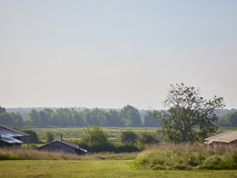 Uitzicht op velden, bomen en hutten bij BoerenBed College Farm vakantiepark in Oost-Engeland, onder heldere lucht.