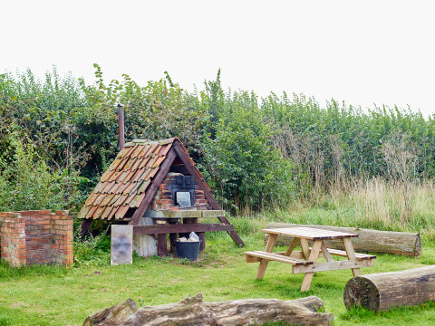 Buiten picknickplek met oven onder pannendak, houten tafel en banken bij BoerenBed College Farm.