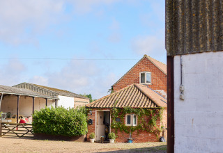 Rød murstensbygning med klatreplanter, gårdsplads og udhus på BoerenBed College Farm, Østengland.