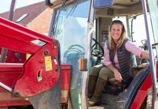 Mujer sonriente en un tractor en BoerenBed College Farm, un parque vacacional en el Este de Inglaterra, Reino Unido.