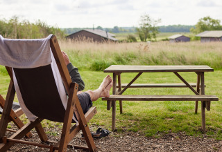 Entspannte Szene auf der BoerenBed College Farm in Ostengland mit Person auf Liegestuhl am Picknicktisch.