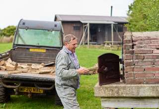 Man stopt brandhout in een buitenoven bij BoerenBed Billingsmoor Farm in Zuidwest-Engeland.