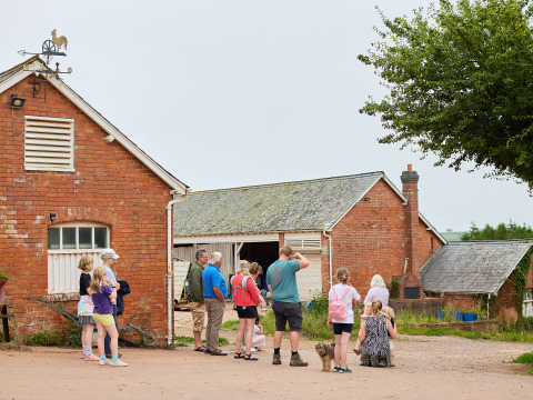 Families with children and pets gather outside red brick farm buildings at BoerenBed Billingsmoor Farm, UK.