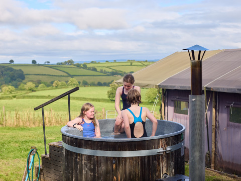 Three children enjoy an outdoor hot tub at BoerenBed Billingsmoor Farm holiday park in scenic South West England.