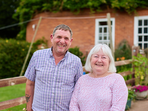 Et smilende ældre par står foran et hegn på BoerenBed Billingsmoor Farm i det sydvestlige England.