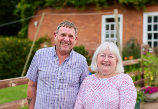 Un couple âgé souriant se tient devant une clôture à BoerenBed Billingsmoor Farm, dans le sud-ouest de l’Angleterre.