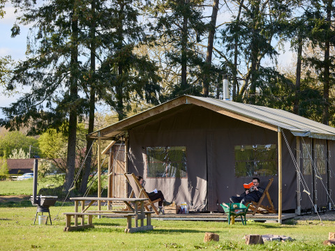 Persoon leest buiten voor een grote tent bij BoerenBed Foxglove farm, omringd door bomen in Zuidoost-Engeland.
