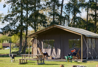 Persoon leest buiten voor een grote tent bij BoerenBed Foxglove farm, omringd door bomen in Zuidoost-Engeland.