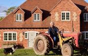 Oudere man op rode tractor voor bakstenen huis met hond aan zijn zijde bij BoerenBed Foxglove farm.
