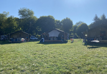 Three safari tents at Campsite La Faz in France, surrounded by green grass and trees under a clear sky.