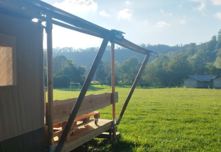 View from a safari tent porch overlooking a green meadow with hills and trees in the sunny distance.