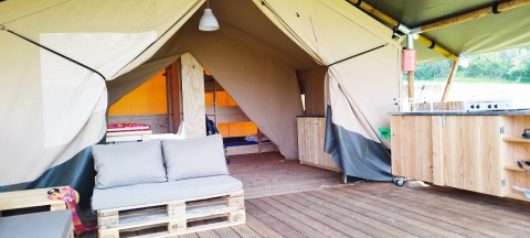 Foto interior de una tienda safari de lujo en el camping La Faz en Francia, con sofá de palets y cocina.