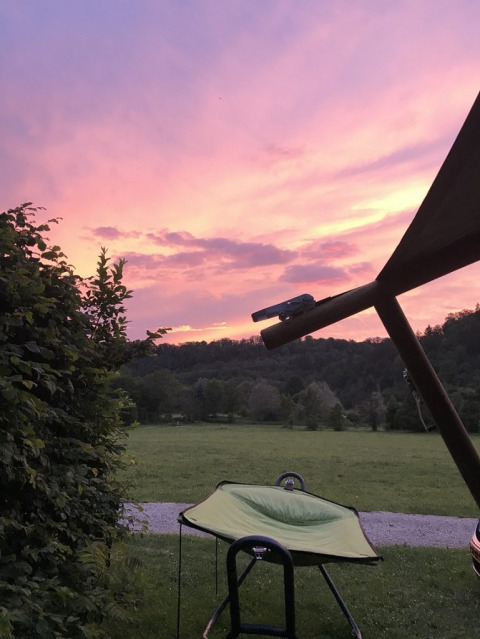 Safari tent overlooking a green field and forest, with a beautiful pink and purple sunset in the sky.
