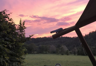 Safari tent overlooking a green field and forest, with a beautiful pink and purple sunset in the sky.