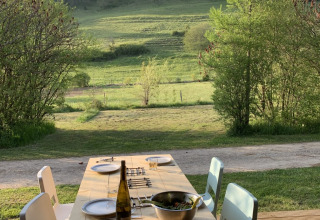Table de salle à manger en bois à l'extérieur, quatre chaises, bouteille de vin, salade et vue verdoyante.