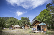 Tienda safari Trappeur en Huttopia Bourg Saint-Maurice, Francia, rodeada de montañas y árboles verdes.
