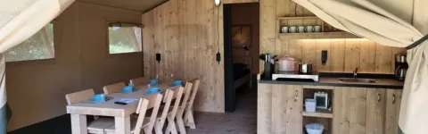 Interior of Lodgetent XL with bathroom at Campsite La Faz, France, featuring dining table and kitchen.