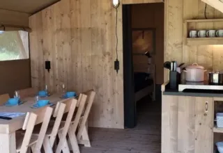 Interior of Lodgetent XL with bathroom at Campsite La Faz, France, featuring dining table and kitchen.