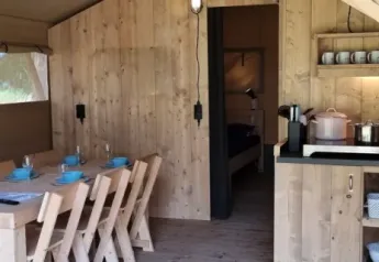 Interior of Lodgetent XL with bathroom at Campsite La Faz, France, featuring dining table and kitchen.