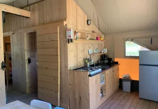 Vue intérieure d'une tente safari avec panneaux en bois, petite cuisine, table à manger et réfrigérateur.