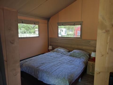 Vue intérieure d'une tente safari avec un lit double, des fenêtres et des tables de chevet avec lampes.