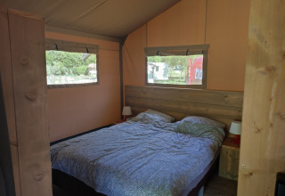Vue intérieure d'une tente safari avec un lit double, des fenêtres et des tables de chevet avec lampes.