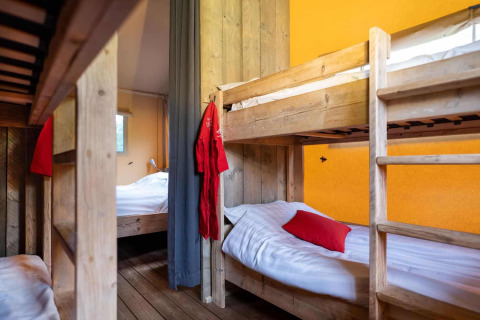 Interior of Lodgetent XL with wooden bunk beds and yellow wall at Campsite La Faz in France.