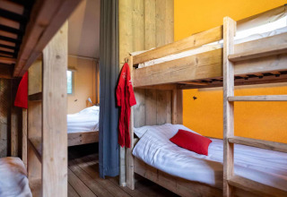 Interior of Lodgetent XL with wooden bunk beds and yellow wall at Campsite La Faz in France.