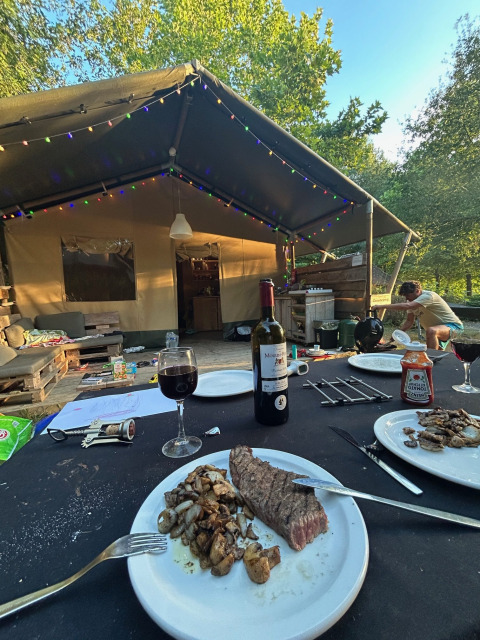 Dinner with steak and wine in front of a safari tent, with string lights and a cozy outdoor vibe.