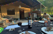 Dinner with steak and wine in front of a safari tent, with string lights and a cozy outdoor vibe.