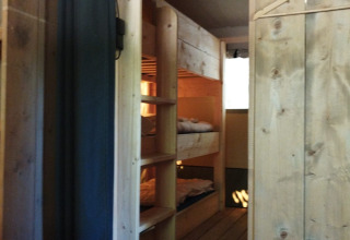 Wooden interior of a safari tent bedroom featuring bunk beds and shelves, perfect for outdoor stays.