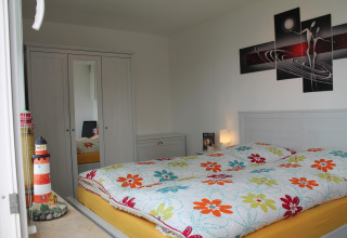 Slaapkamer in lodge 'Am Strand' in Duitsland met bloemenbedsprei en vuurtorendecoratie.