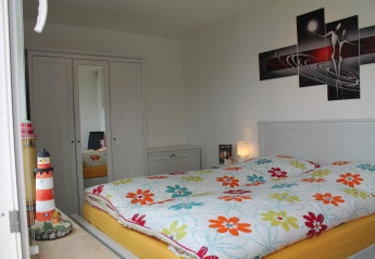 Bedroom at lodge 'Am Strand' in Germany featuring a floral bedspread and lighthouse decoration.