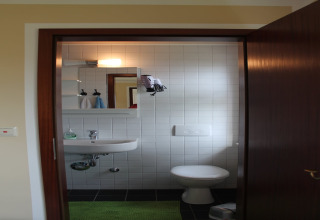 Kleine badkamer bij lodge «Am Strand» in Duitsland met wasbak, toilet en spiegel tegen witte tegels.