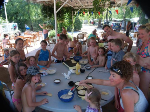 Bambini e adulti cucinano insieme all'aperto su un grande tavolo al campeggio La Digue in Francia.