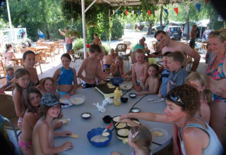 Bambini e adulti cucinano insieme all'aperto su un grande tavolo al campeggio La Digue in Francia.