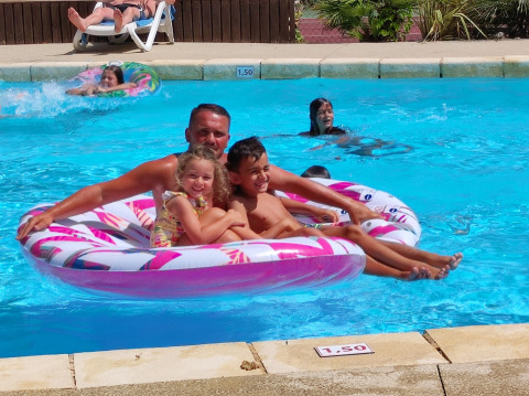 Un uomo e due bambini sorridenti su un gonfiabile rosa nella piscina del campeggio La Digue in Francia.