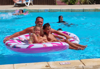Un uomo e due bambini sorridenti su un gonfiabile rosa nella piscina del campeggio La Digue in Francia.